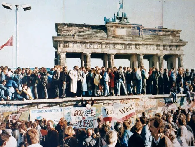 Menschen feiern im November 1989 auf der Berliner Mauer vor dem Brandenburger Tor